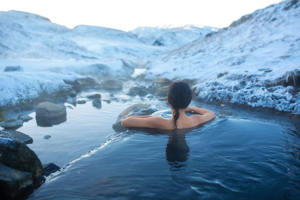 The girl bathes in a hot spring in the open air with a gorgeous view of the snowy mountains. Incredible iceland in winter.