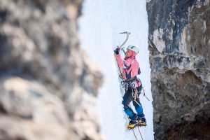 girl mountaineer climbing a frozen waterfall and smiling